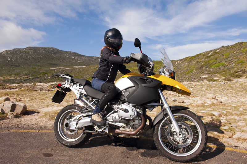 蓝天白云下山林间公路上骑着戴着头盔的黑色摩托车的女子