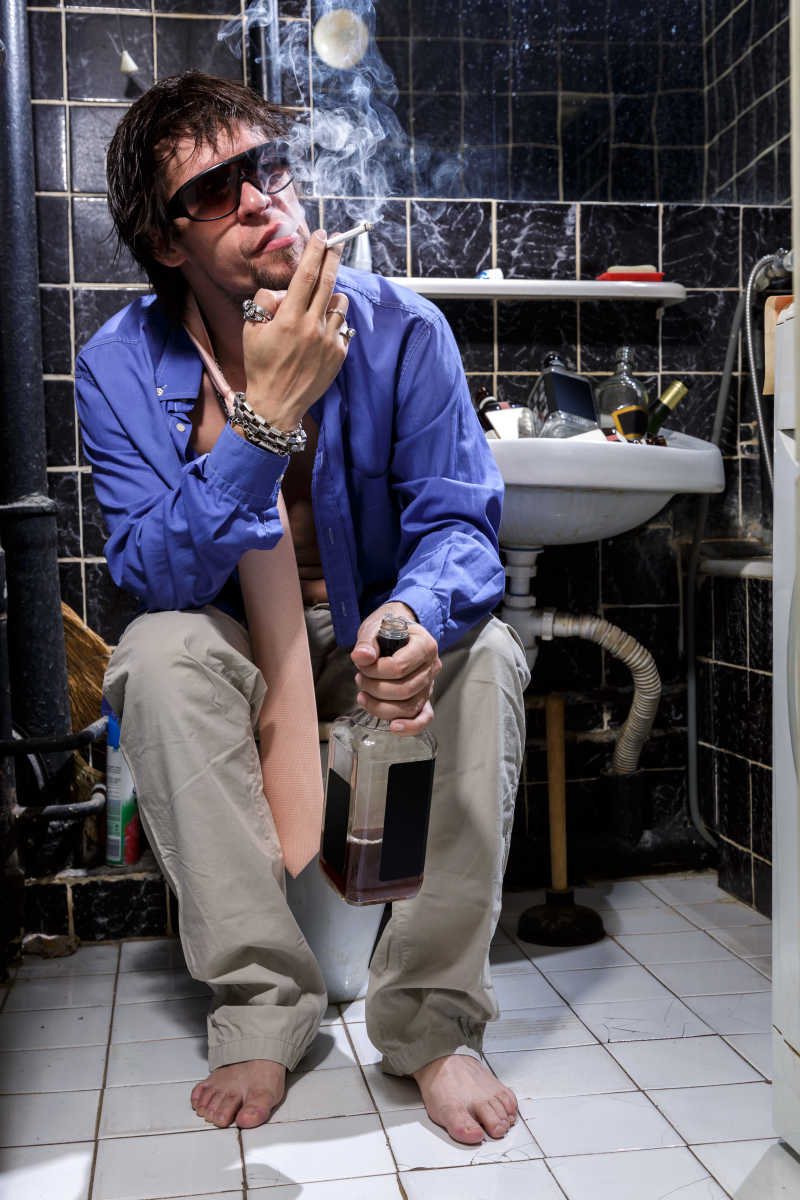厕所内光着脚丫一边吸烟一边喝酒的男人