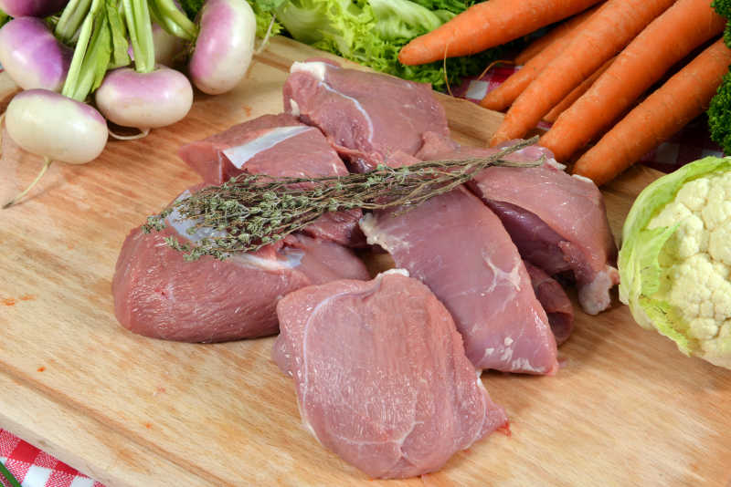 厨房里蔬菜背景下的砧板上的生猪肉块