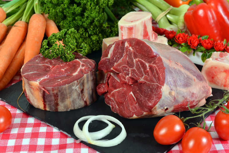 红色桌布上的一块红色的牛瘦肉和一些蔬菜
