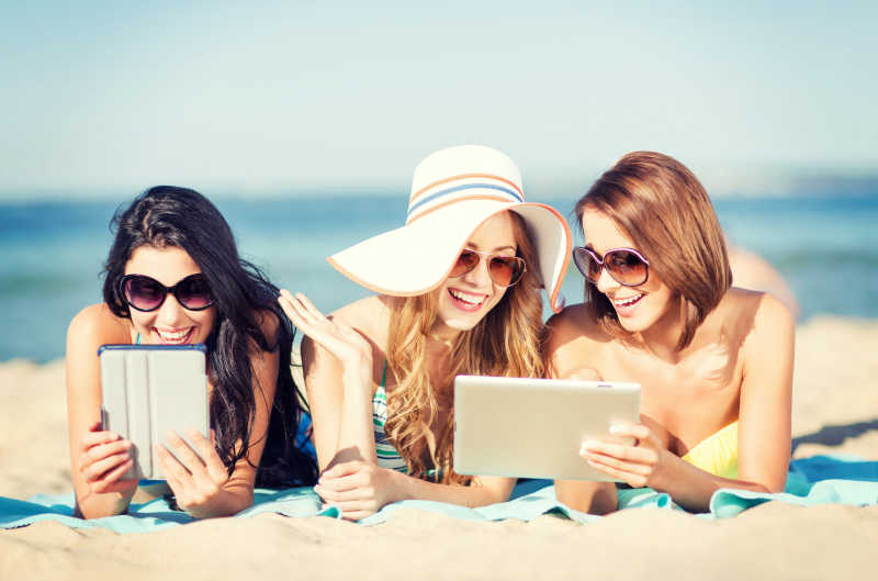海滩上拿着平板电脑大笑的女孩们