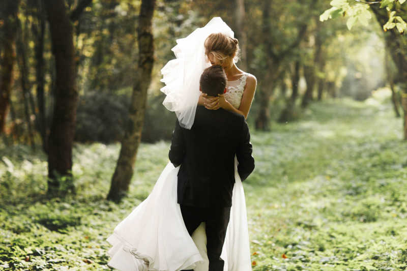 阳光森林中浪漫亲吻的新娘和新郎