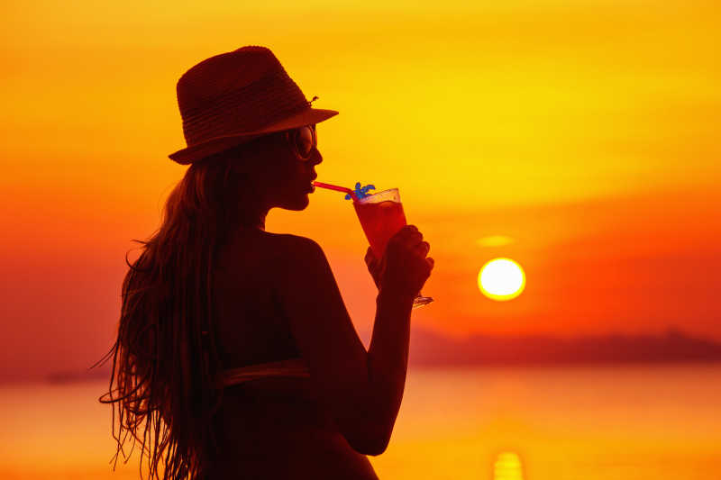 在落日的海边喝着鸡尾酒的美女