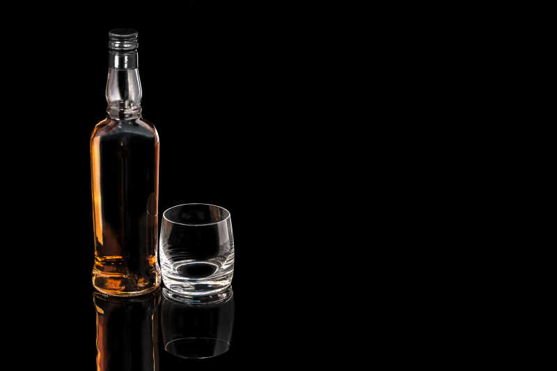 一瓶威士忌和一个黑色背景的空杯子