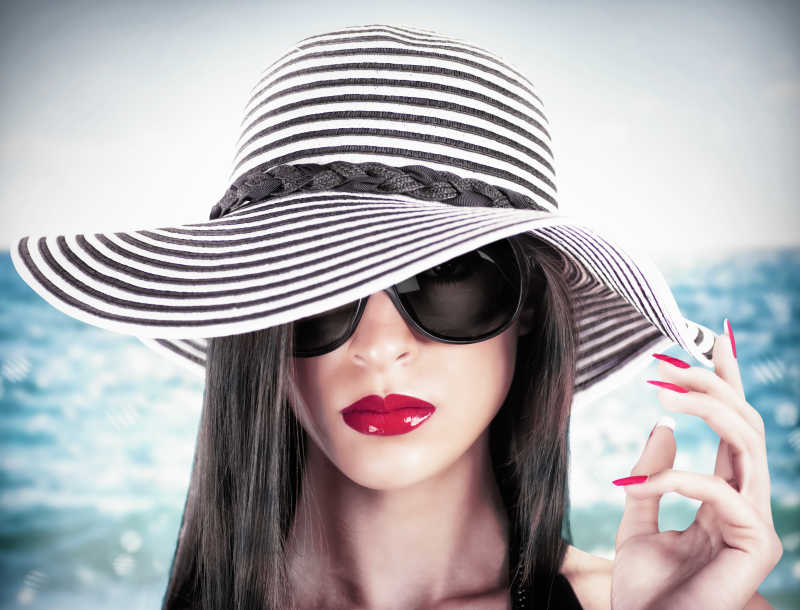 海滩上戴帽子和太阳镜的红唇美女