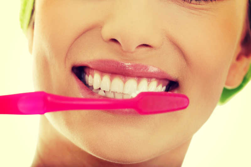 黄色背景下使用红色牙刷刷牙的微笑的女人