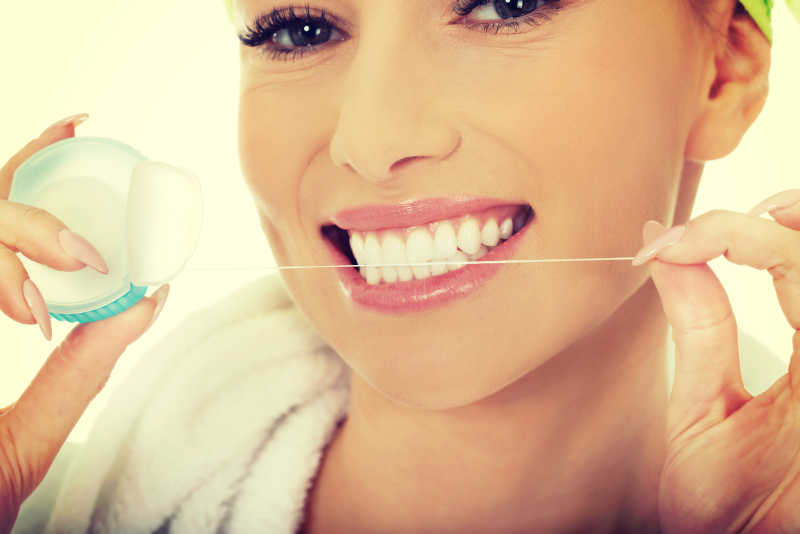 美丽的女人在使用牙线清洁她的洁白的牙齿