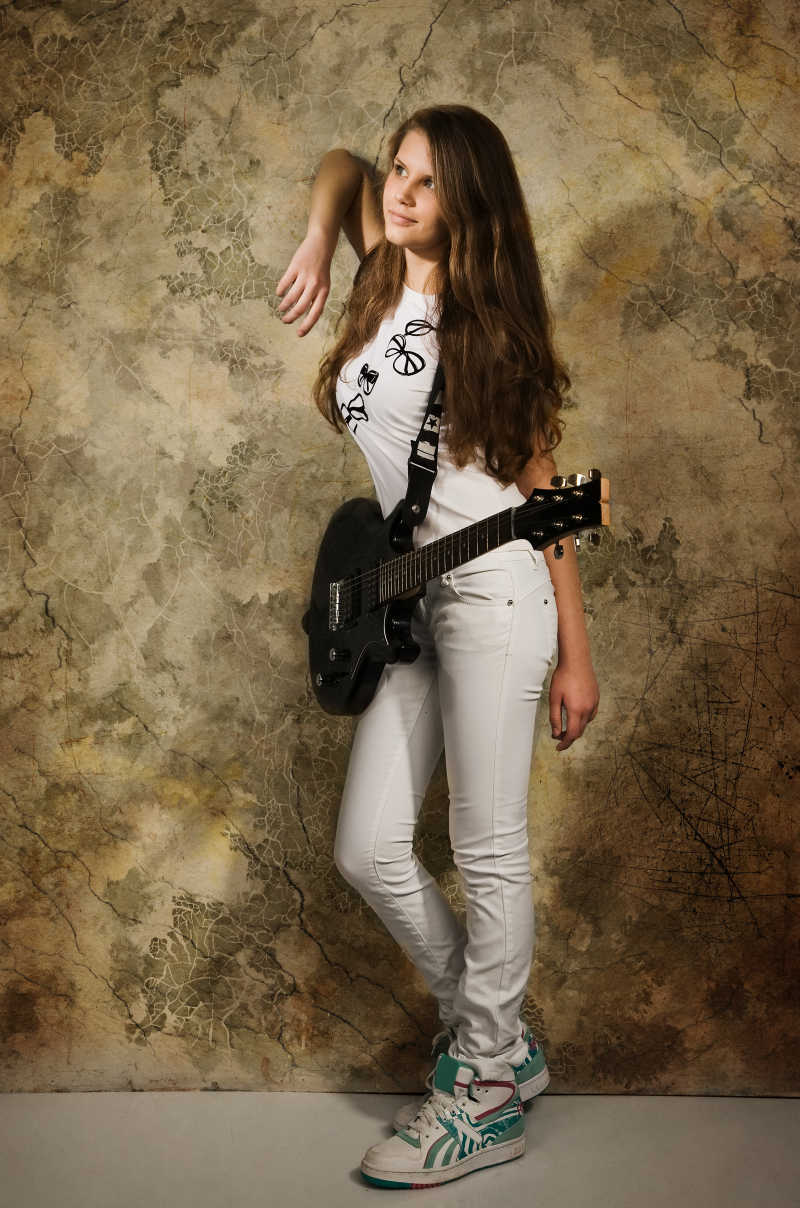 身上背着吉他的女孩靠着墙