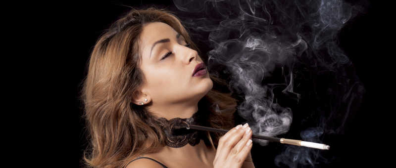 黑色背景下吸着带烟嘴的香烟的性感女人
