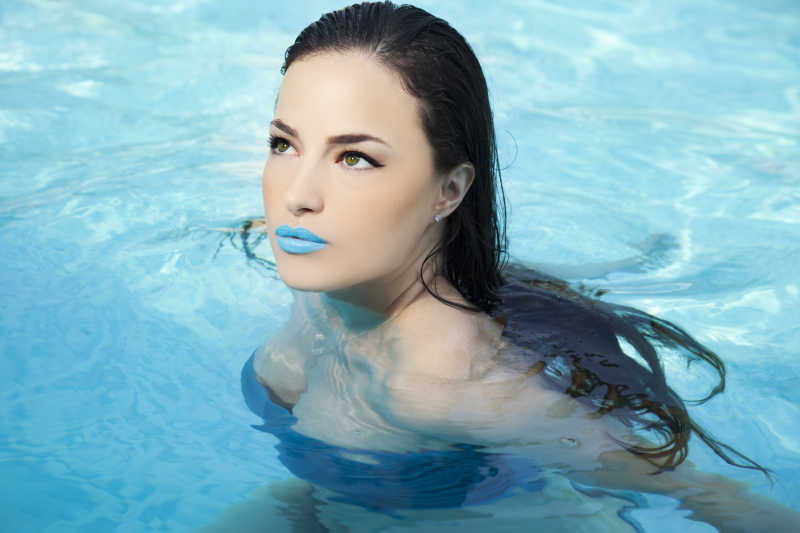 蓝色嘴唇的性感女人在游泳池中