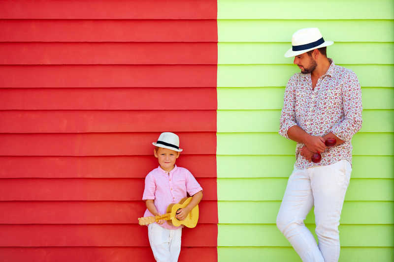 彩色墙上的父亲看着儿子演奏乐器