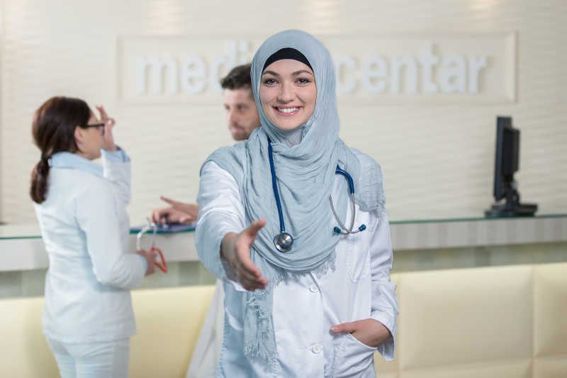 年轻微笑的伸出一只手的女穆斯林医生