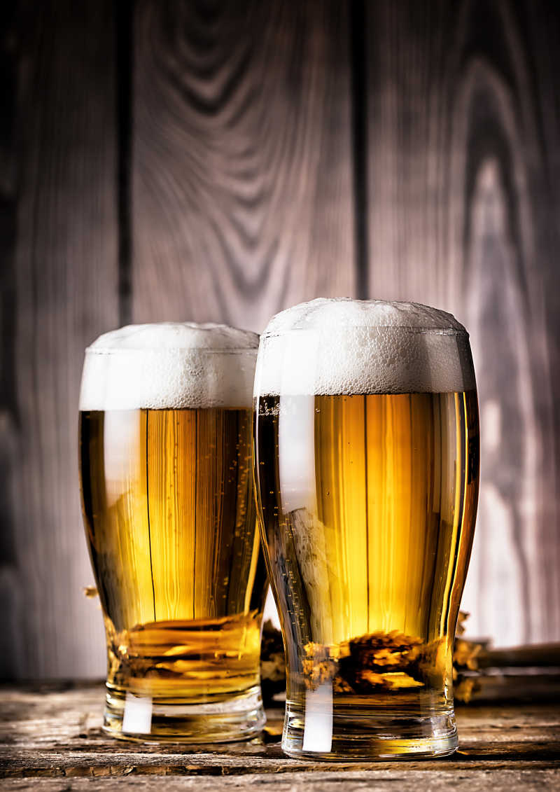 木质背景下两杯新鲜的泡沫啤酒