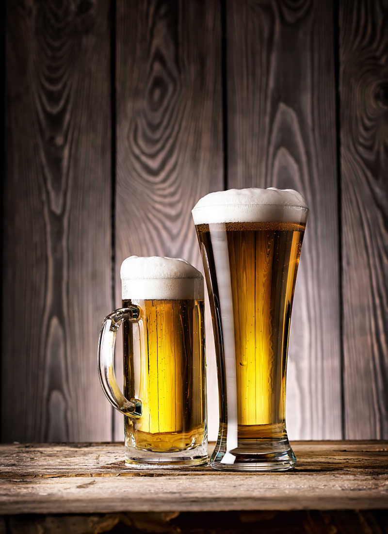 木制背景下放在木桌上的两玻璃杯泡沫啤酒