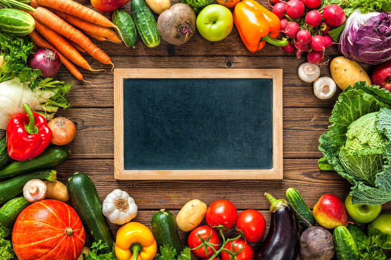 木桌上围绕黑板的新鲜的胡萝卜蔬菜辣椒圆白菜等水果蔬菜