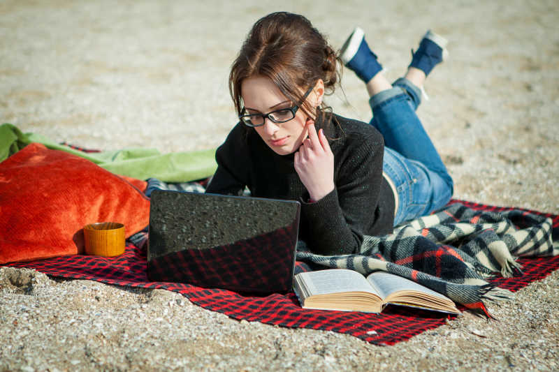 沙滩上趴着使用笔记本电脑的年轻美女