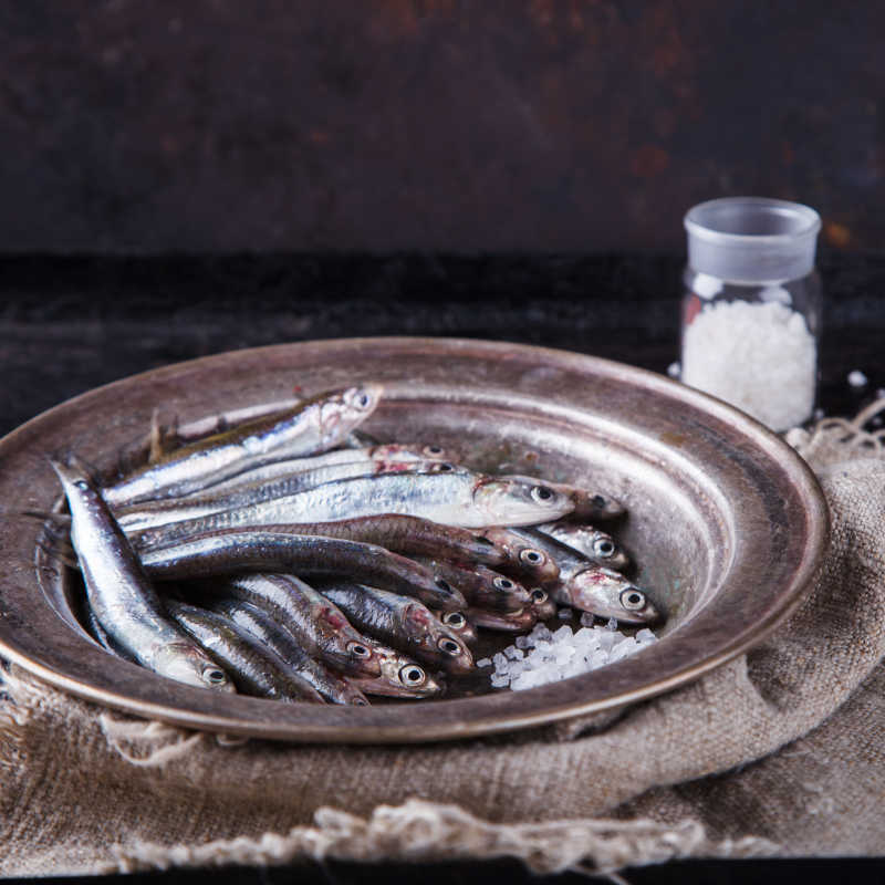 亚麻布上圆形盘子里装着的鳀鱼和白色颗粒状调味料