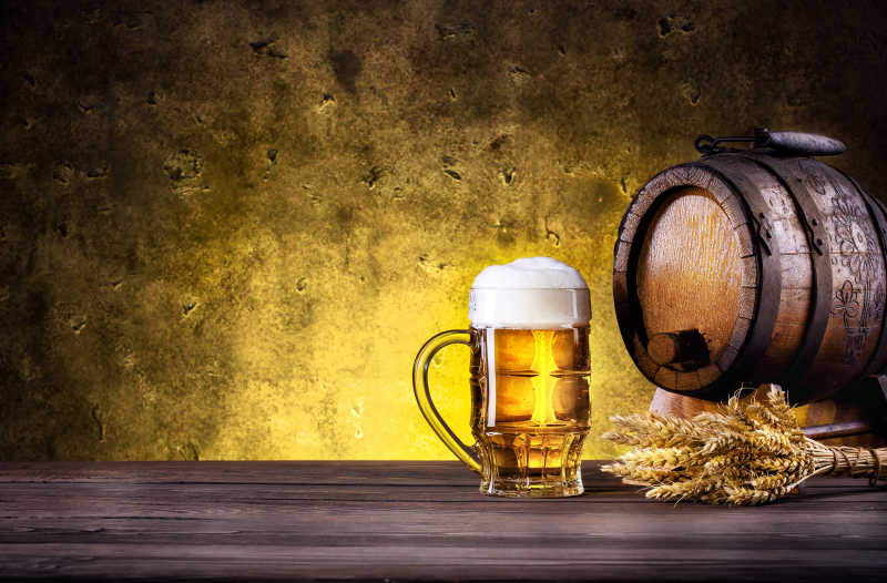 老旧背景下的木桶和泡沫啤酒以及金黄的麦穗