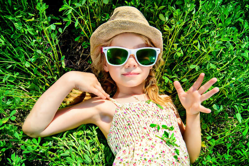 绿色草地上躺在草地上戴着太阳镜和遮阳帽的小女孩