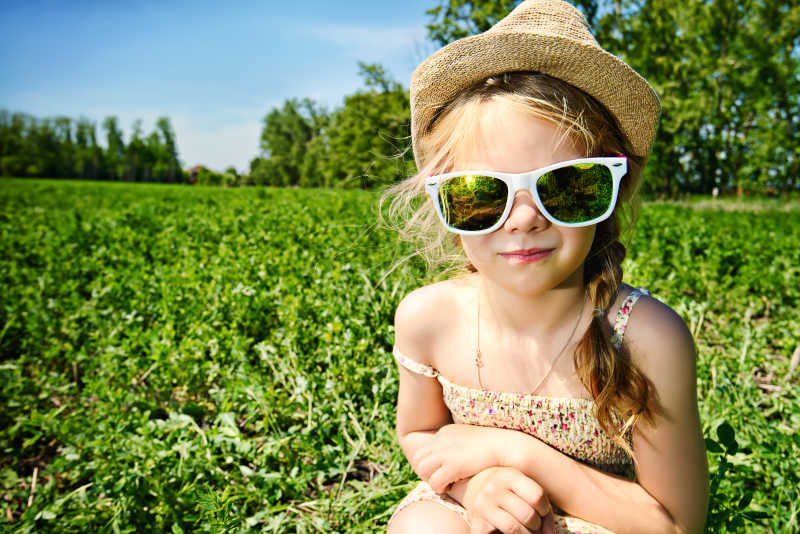 蓝天下草地上戴着太阳镜的小女孩