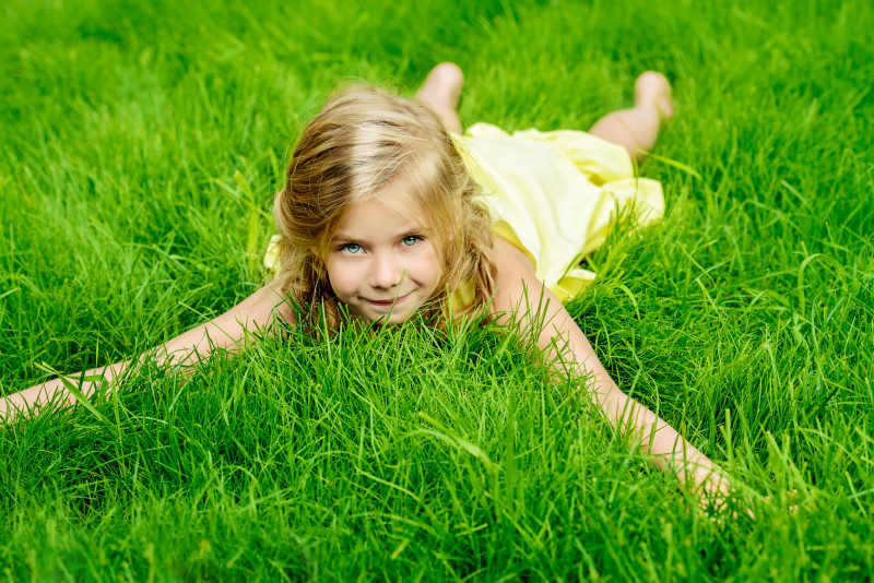 在绿色草地上趴着的金发小女孩