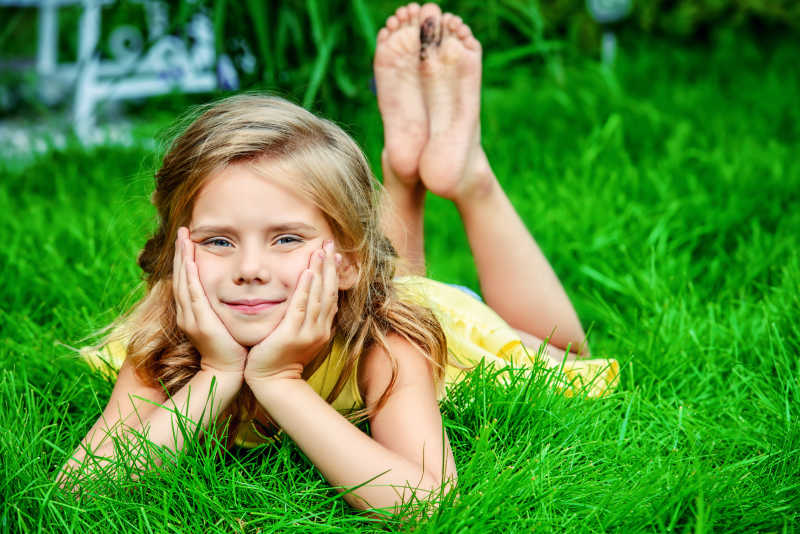 绿色植物背景下手托着腮趴在草地上的小女孩