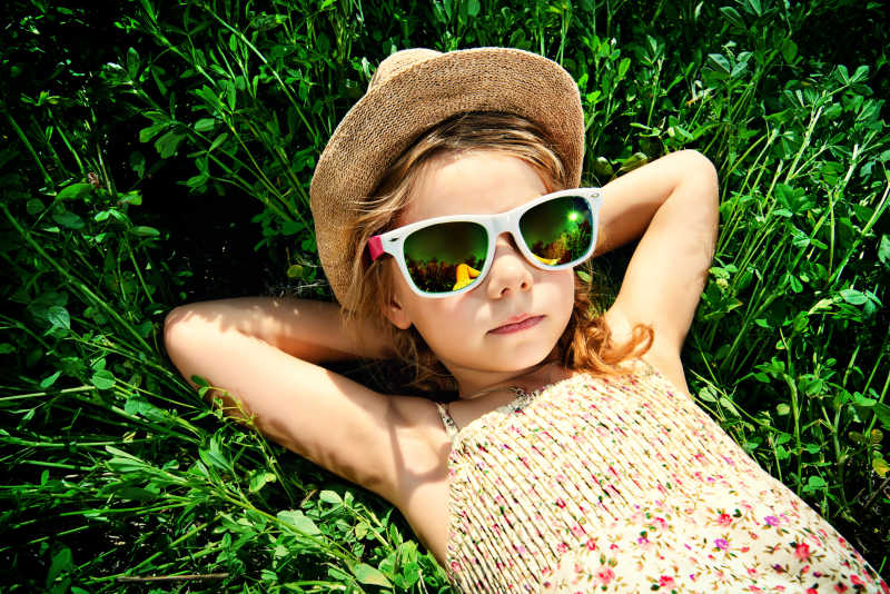 阳光下戴着太阳镜躺在草地上的小女孩