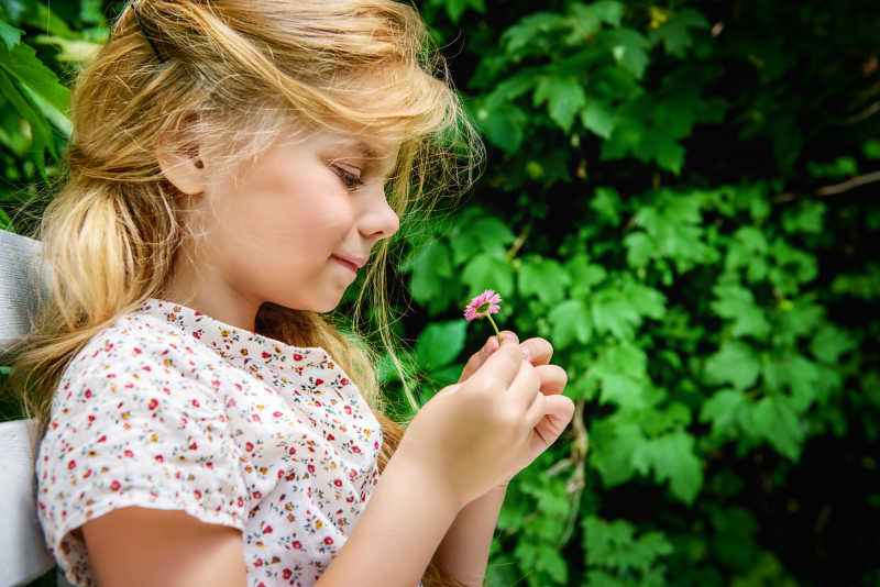 绿色植物背景下拿着一朵小花的金发小女孩