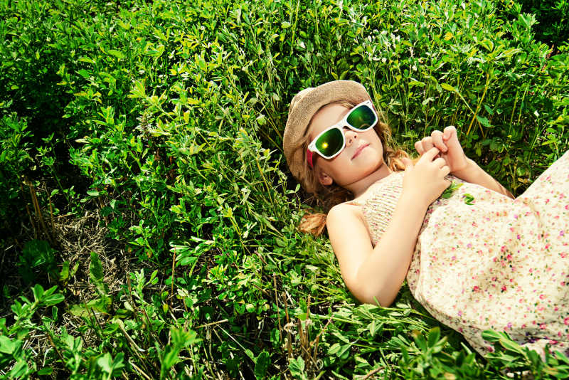 阳光下躺在草地上戴着太阳镜的小女孩