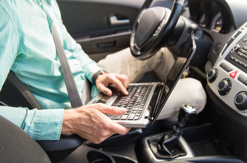 驾驶汽车的男性使用笔记本电脑