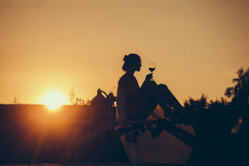 在傍晚的夕阳下喝着葡萄酒的美女剪影