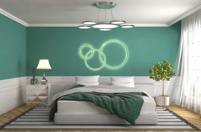 卧室床后绿色墙壁背景上的绿色圆环装饰和床旁的绿植及台灯