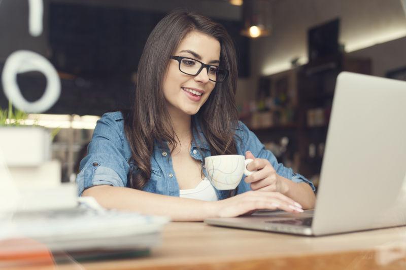 坐在咖啡馆喝咖啡玩笔记本电脑的女人