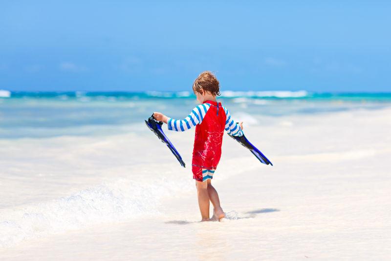 在海边拿着潜水脚板玩耍的小男孩
