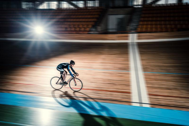 黑夜在有灯的体育馆在跑道上骑自行车的运动员