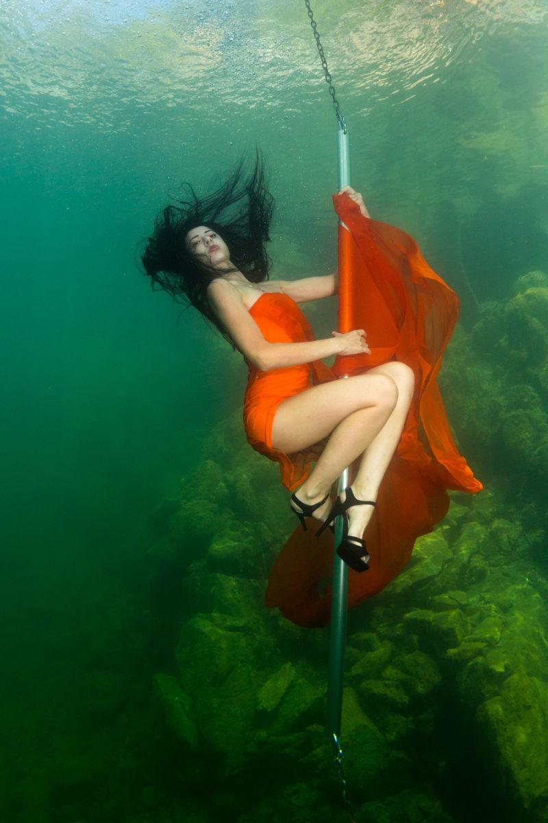 穿着红色连衣裙跳脱衣舞的年轻女子在水下