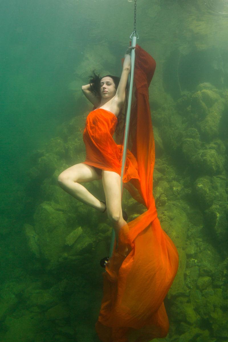 穿着红色裙子在水下跳脱衣舞的美丽的窈窕女孩