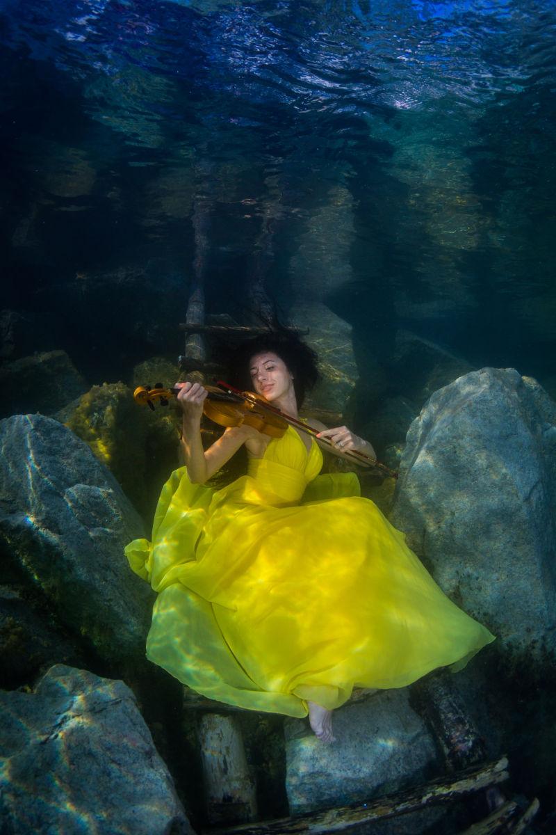 摆在湖边楼梯上的穿着一件裙子的年轻的优雅女人拿着小提琴