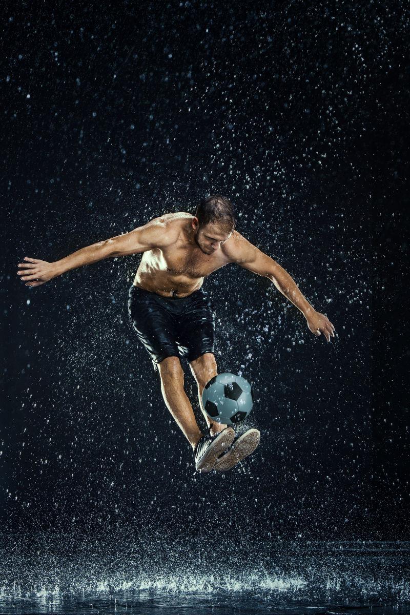 黑色背景下空中踢足球的运动员周围的水滴