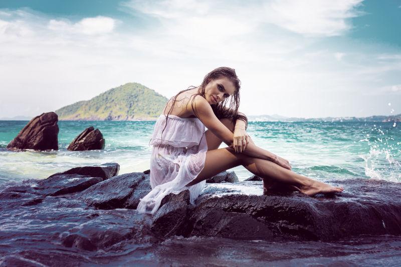 坐在海边岩石的年轻美女