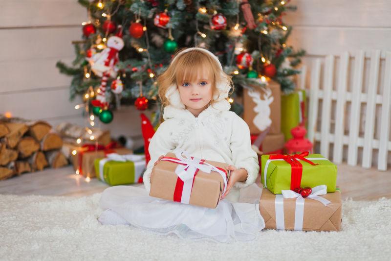 圣诞树旁边的小女孩手里拿着礼物