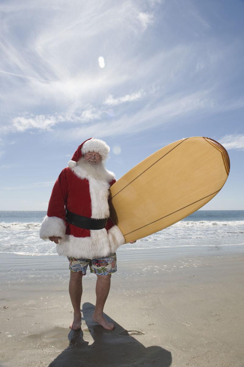 沙滩上拿着冲浪板的圣诞老人