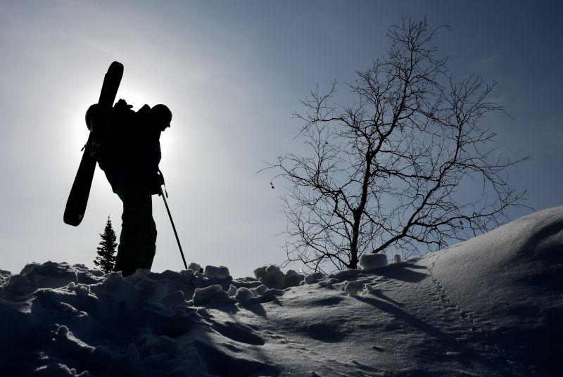 晴天阳光下站在雪地上的背着装备滑雪的人剪影