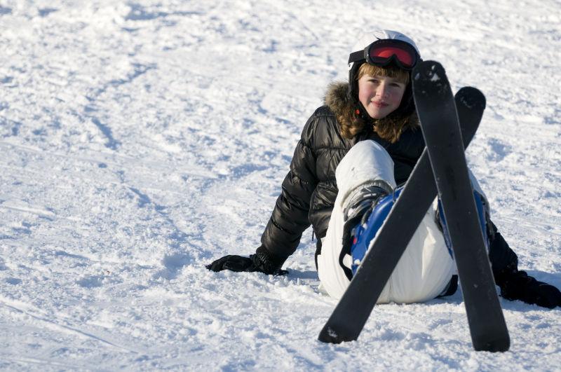 阳光下坐在雪地上穿着滑雪板的女孩