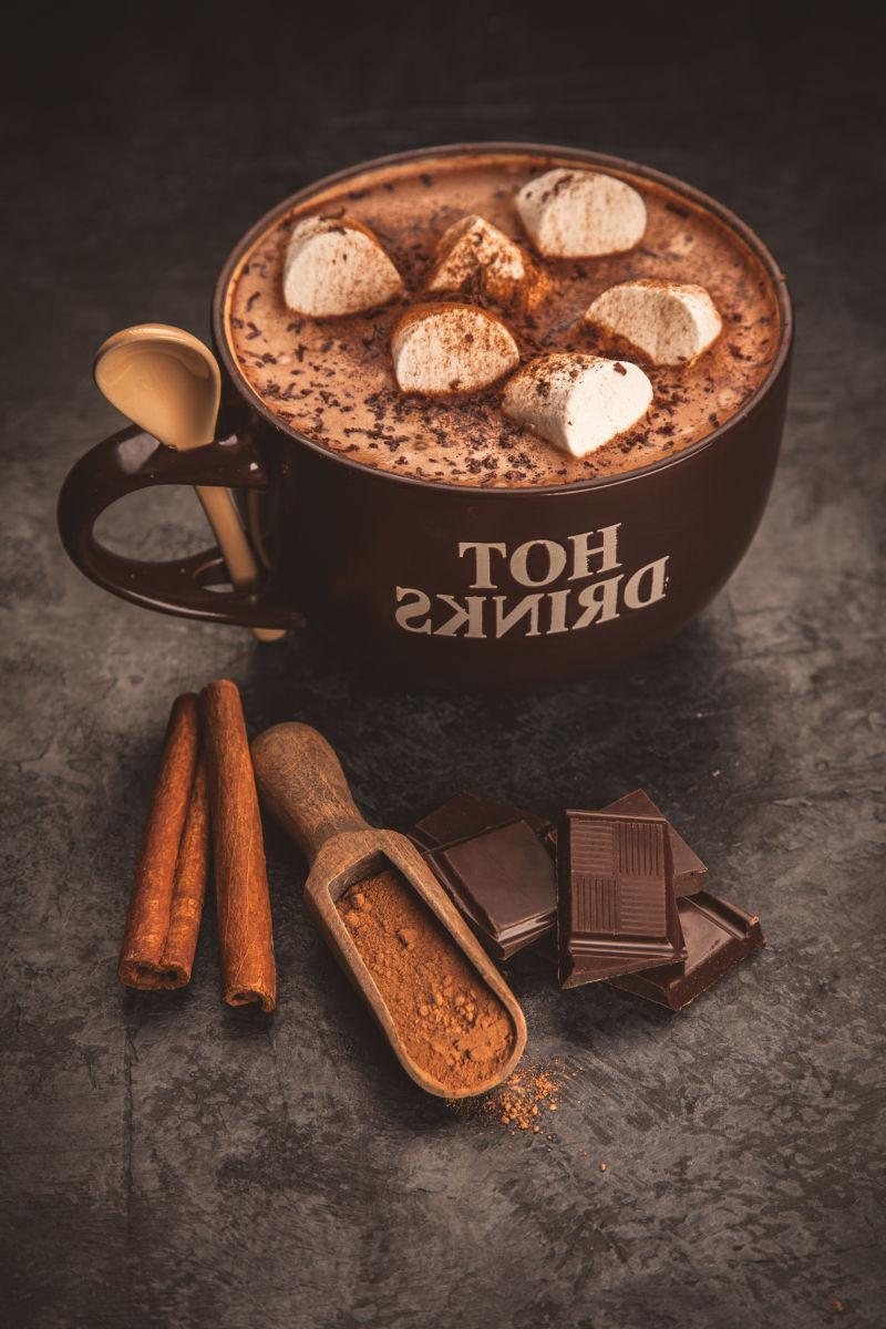 黑色背景下的一杯带有棉花糖的热巧克力和肉桂棒