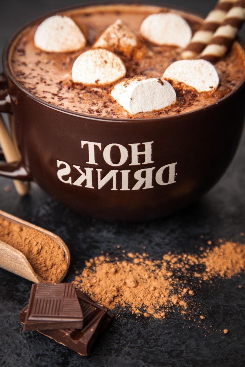 黑色桌上的一杯带有棉花糖的热巧克力和散落的可可粉