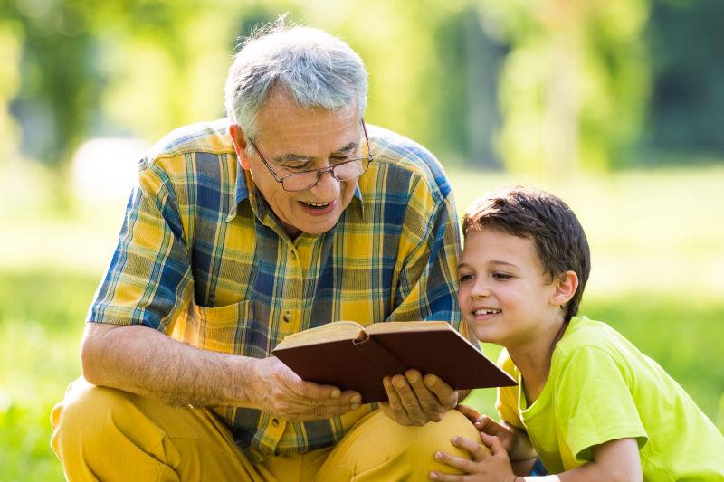 公园里祖父陪着小外孙在看书