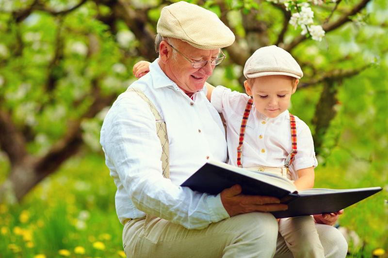 公园里祖父抱着小男孩在看书