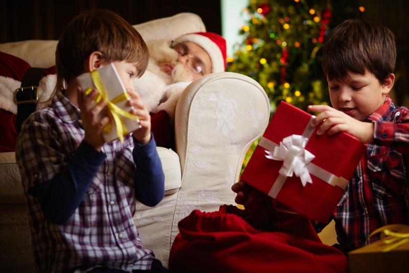 躺在沙发上的圣诞老人和拿着礼物的两个小男孩