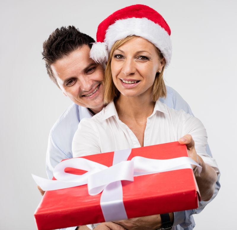 灰色背景上开心的拿着圣诞礼物的青年夫妇